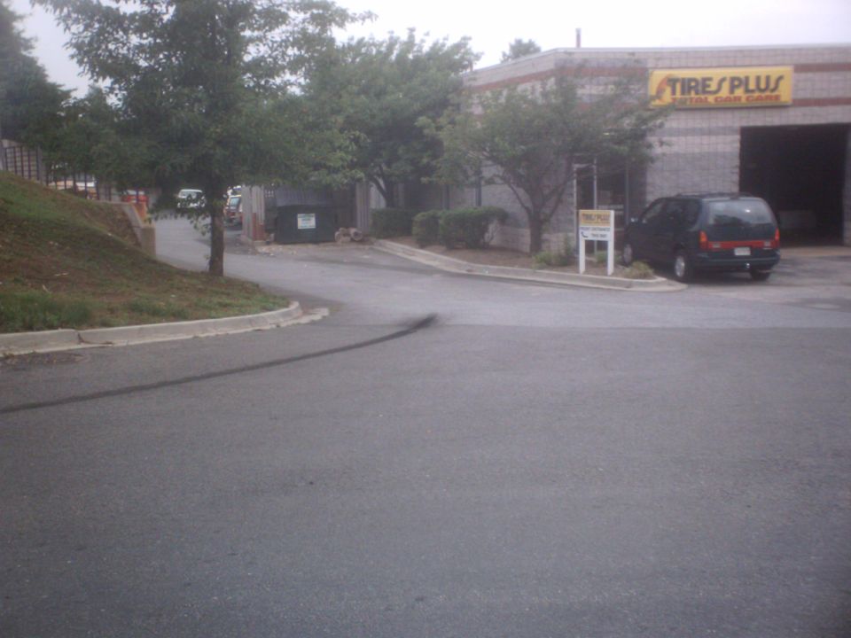 Dark minivan parked outside a Tires Plus auto shop with open garage bay