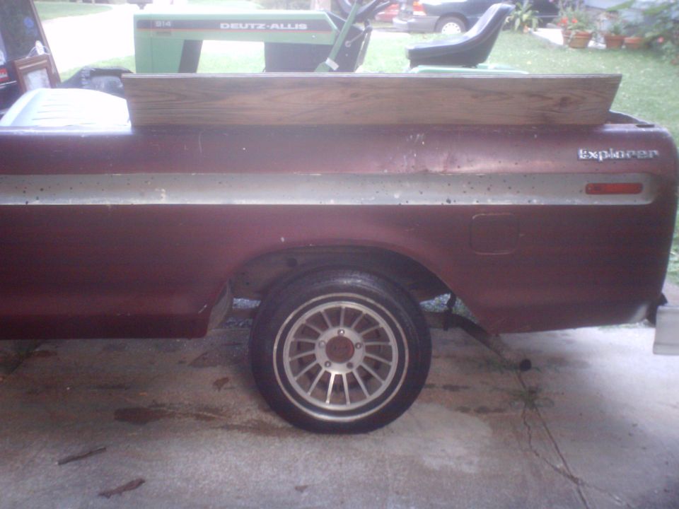 Maroon Ford pickup bed with Explorer badge and slotted alloy wheel, wooden board on top, Deutz-Allis tractor behind