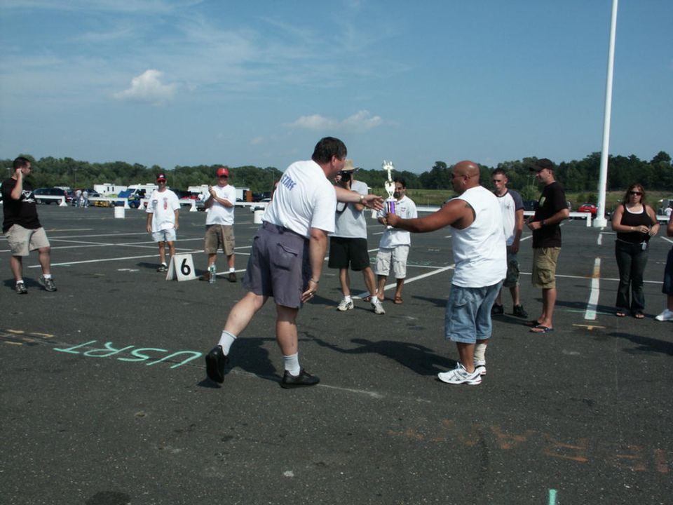 People receiving a trophy at a car show, with cars in the background