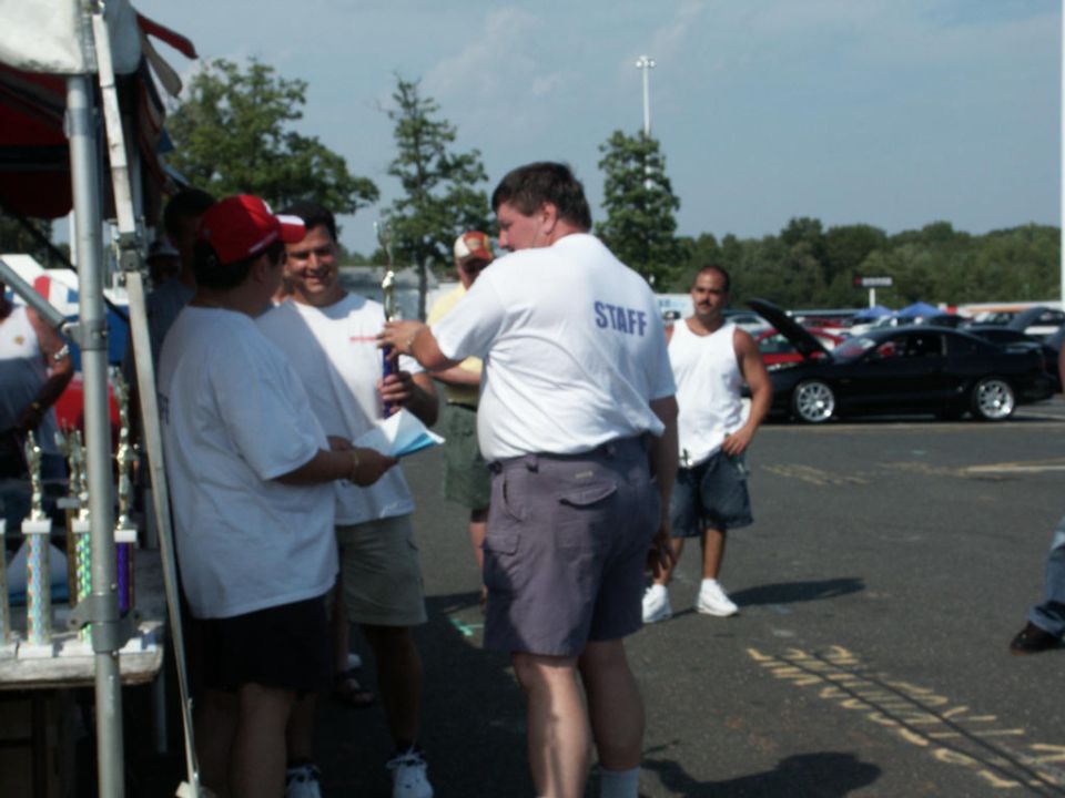 People receiving trophies at a car show, with cars parked in the background