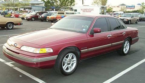 1992 Ford Crown Victoria - A red 1992 Ford Crown Victoria sedan is parked in a lot with other vehicles.