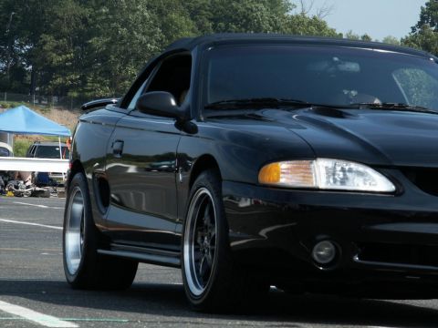 2001 Mercury Grand Marquis - A black convertible Mustang is parked on asphalt with trees in the background and a blue tent to the left.