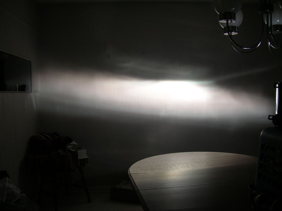 Headlight beam pattern projected onto a wall, with a table in the foreground and a chandelier above