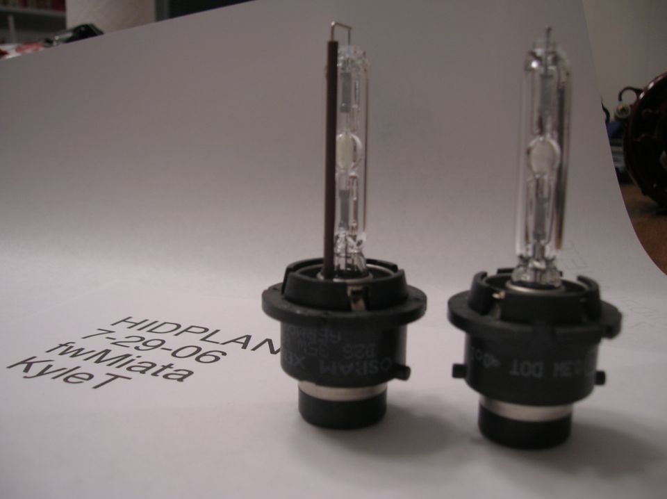 Two HID headlight bulbs on paper with text 'HIDPLAN 7-29-06 fwMiata Kyle T'