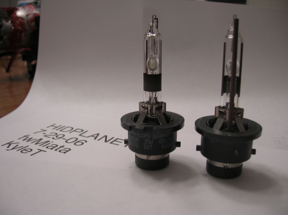 Two HID bulbs on a white surface with handwritten text and a SuperMotors logo