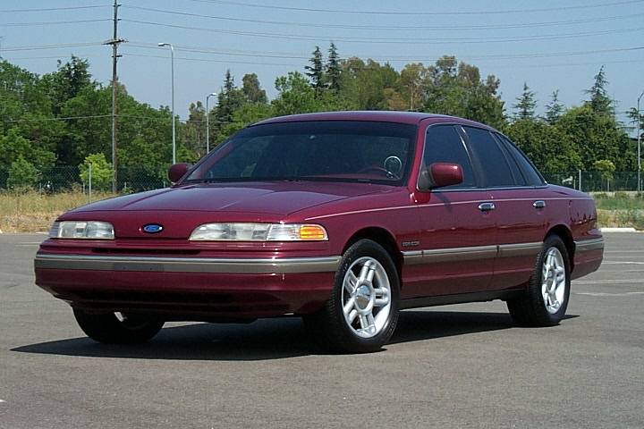 Maroon Ford Crown Victoria sedan parked in empty lot, front 3/4 view