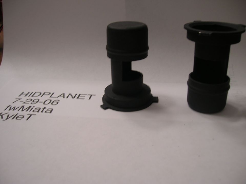 Two black plastic dust caps for car headlights on a white surface with text