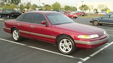 1992 Ford Crown Victoria - A dark red/maroon Ford Crown Victoria full-size sedan viewed from the front three-quarter angle, parked in an outdoor lot with alloy wheels…
