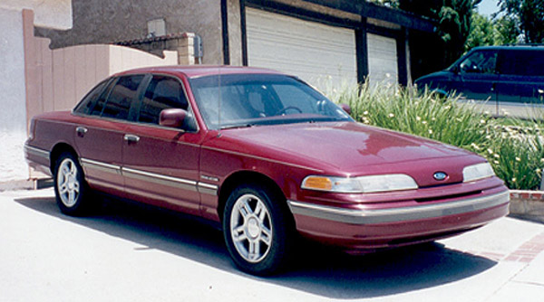 Maroon four-door Ford sedan, front 3/4 view, parked in driveway