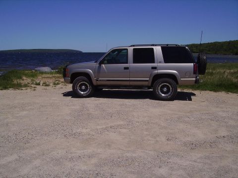 2000 Chevrolet Tahoe - Side view of a silver Chevrolet Tahoe parked near a lake on a sunny day.