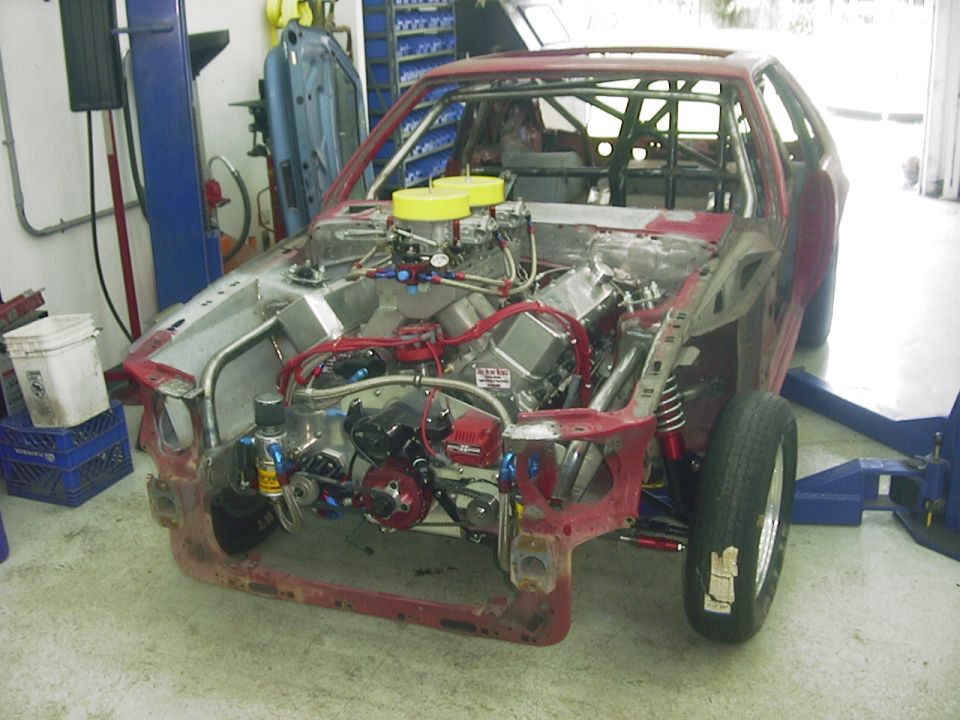 Custom race car with engine exposed, roll cage visible, in a workshop
