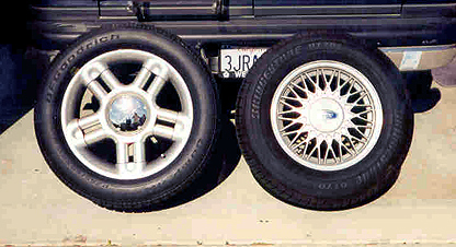 1992 Ford Crown Victoria - Two tires and wheels leaned against a truck for comparison: a five-spoke alloy and a fine-mesh wheel, with a California plate behind.