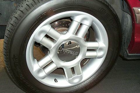 1992 Ford Crown Victoria - Close-up of a five-spoke silver alloy wheel with a chrome 'Fittipaldi' center cap, mounted with a BFGoodrich tire on a dark red vehicle. Th…