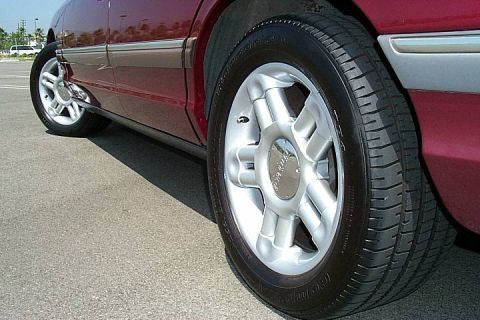 1992 Ford Crown Victoria - Close-up of the front passenger-side wheel on a dark red/maroon Ford sedan, showing a silver five-spoke alloy wheel with a Ford center cap…