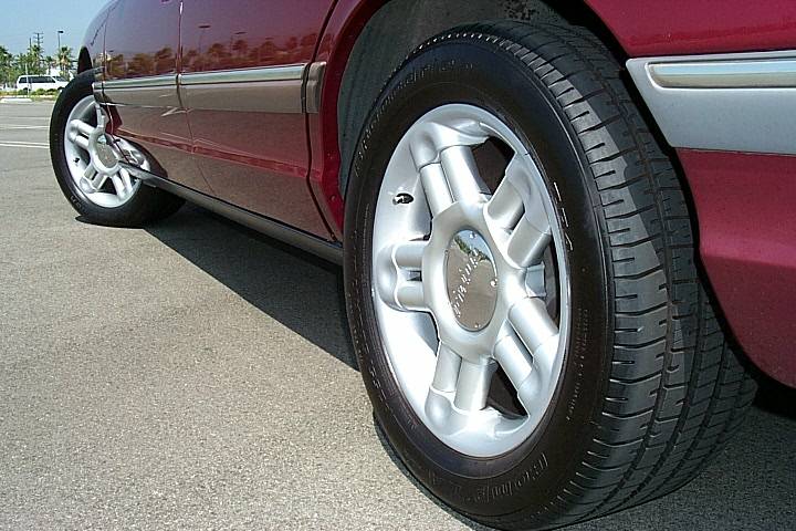 Silver five-spoke alloy wheel and tire on a maroon Ford sedan