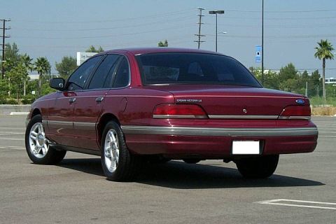 1992 Ford Crown Victoria - A dark red/maroon Ford Crown Victoria LX four-door sedan photographed from the rear driver's side (3/4 rear angle) in a paved parking lot.…