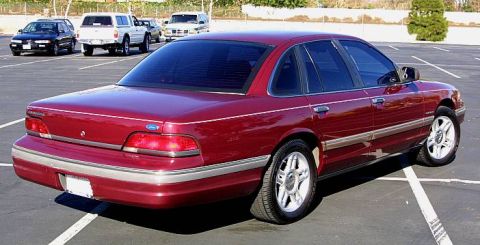 1992 Ford Crown Victoria - A dark red/maroon Ford Crown Victoria full-size sedan viewed from the rear passenger 3/4 angle, parked in an outdoor lot with silver alloy…