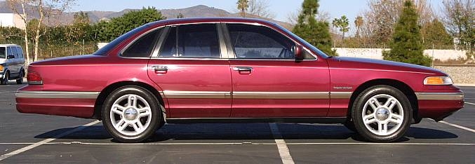 Maroon Ford Crown Victoria sedan, driver-side profile view, parked in empty lot