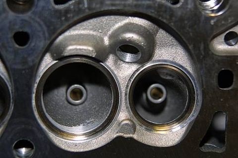 1992 Ford Crown Victoria - Close-up of a bare cast-iron cylinder head combustion chamber showing two machined valve seats and valve guides, with a threaded spark plug…