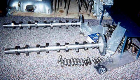 1992 Ford Crown Victoria - Two overhead camshafts laid out on carpet with their timing sprockets, alongside loose valve springs, lifters/followers, a bagged parts kit…