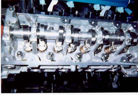 1992 Ford Crown Victoria - Close-up of an overhead-cam aluminum cylinder head with the cam cover removed, showing the camshaft in its bolted bearing caps, roller foll…