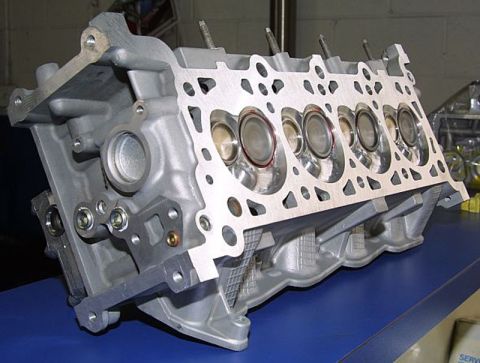 1992 Ford Crown Victoria - Bare aluminum cylinder head sitting deck-face-up on a blue workbench, showing four freshly machined combustion chambers with polished valve…