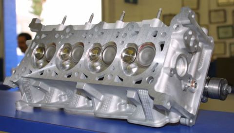 1992 Ford Crown Victoria - Bare aluminum cylinder head sitting upside down on a blue bench, showing four combustion chambers with installed intake and exhaust valves…
