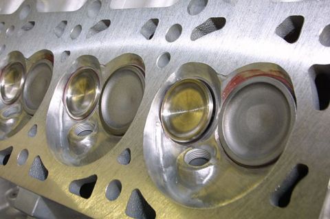 1992 Ford Crown Victoria - An extreme close-up of the combustion-chamber face of an aluminum cylinder head, showing freshly machined intake and exhaust valve seats an…
