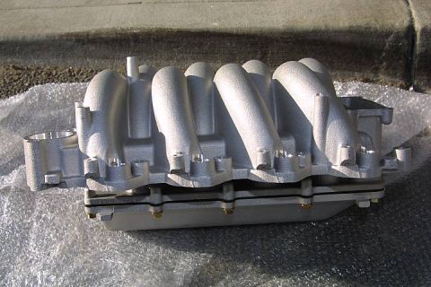 1992 Ford Crown Victoria - A cast aluminum V8 intake manifold sitting on bubble wrap on a concrete step, photographed from the side to show its long curved runners an…