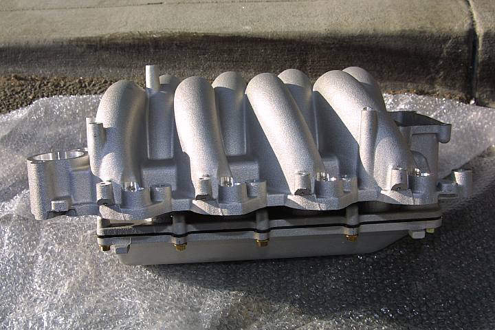 Bare cast aluminum V8 intake manifold on bubble wrap, side view showing runners