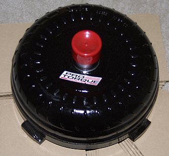 1992 Ford Crown Victoria - New black-painted automatic transmission torque converter sitting face-up on a cardboard box, with a red plastic cap plugging the pilot hub…