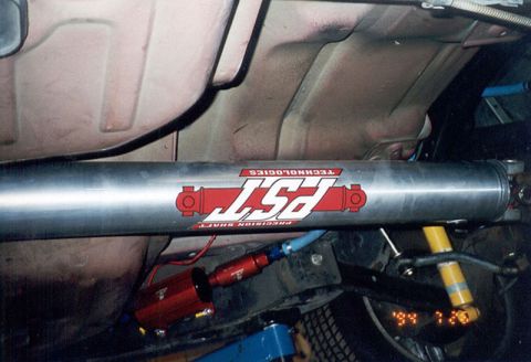 1992 Ford Crown Victoria - An underbody view showing a polished aluminum driveshaft branded 'PST Precision Shaft Technologies,' with a red inline fuel filter, blue br…