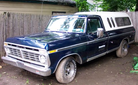 1975 Ford F-150 - This 1975 Ford F-150 pickup features a white camper shell and is parked in a dirt lot.