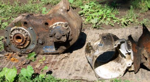 1978 Ford Bronco - This photo shows a heavily rusted transfer case and associated parts resting on the ground.