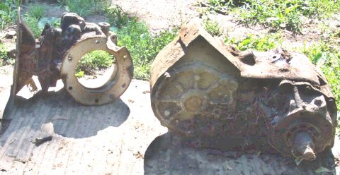 1978 Ford Bronco - Two heavily rusted transfer case parts are laid out on wooden planks in an outdoor setting.