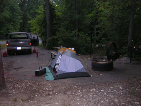 1979 Ford Bronco - A dark pickup truck is parked at a campsite next to a tent and fire pit, with another vehicle visible in the background.