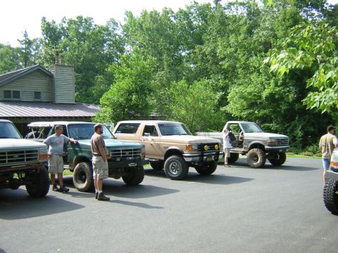 1979 Ford Bronco - Several Ford trucks and a Bronco are parked in front of a building with trees in the background.