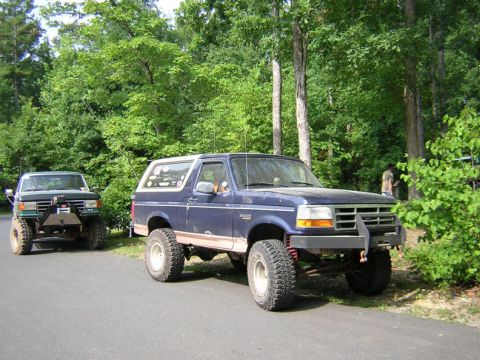 1979 Ford Bronco - A modified blue Ford Bronco is parked on the side of a road, with another off-road vehicle visible behind it.