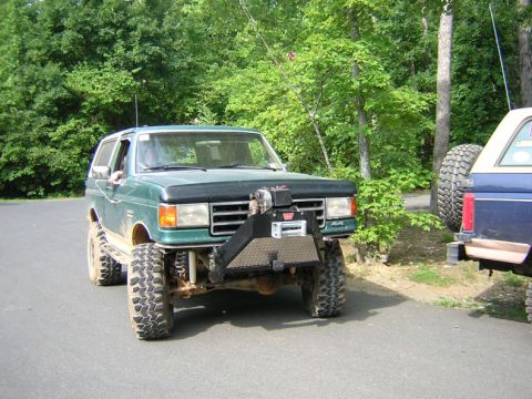1979 Ford Bronco - Modified green Ford Bronco with winch, parked beside another vehicle.
