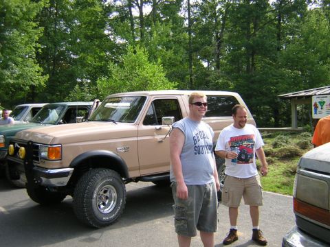 1979 Ford Bronco - A tan 1979 Ford Bronco is parked outdoors with two men standing next to it, and other vehicles are visible in the background.