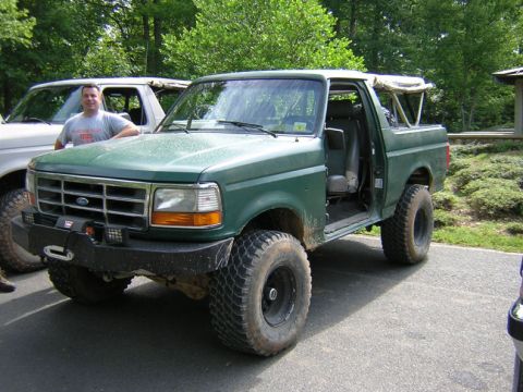 1979 Ford Bronco - Two Ford Broncos parked outdoors, one green with its door open, the other white.