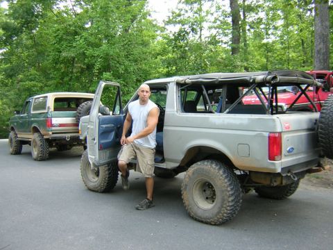 1979 Ford Bronco - A man stands by a modified silver Ford Bronco, with a second green Bronco visible in the background.