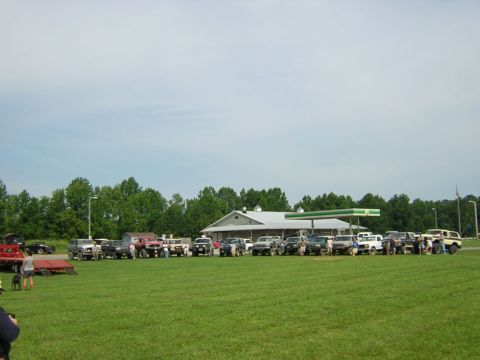 1979 Ford Bronco - A group of 1979 Ford Broncos are gathered on a grassy field in front of a gas station.