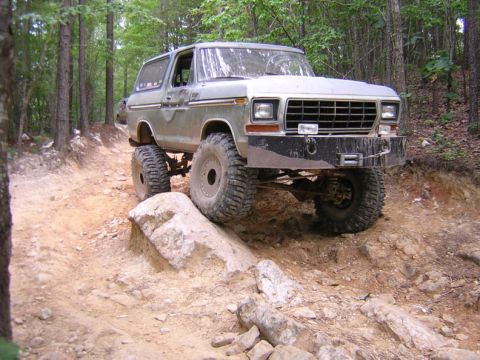 1979 Ford Bronco - A lifted Ford Bronco navigates a rocky off-road trail, its tires gripping the terrain.