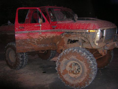 1979 Ford Bronco - This heavily modified red Ford Bronco is caked in mud, showing its off-road capabilities.