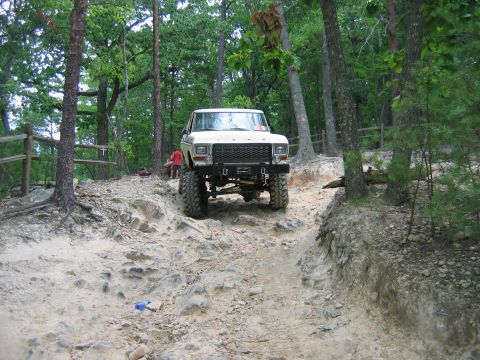 1992 Ford Mustang - A lifted pickup truck navigates a challenging off-road path through a forest.