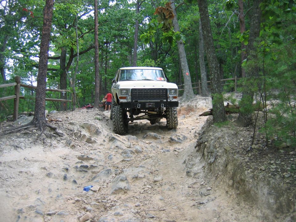 White pickup truck with large tires driving on a rocky, wooded trail