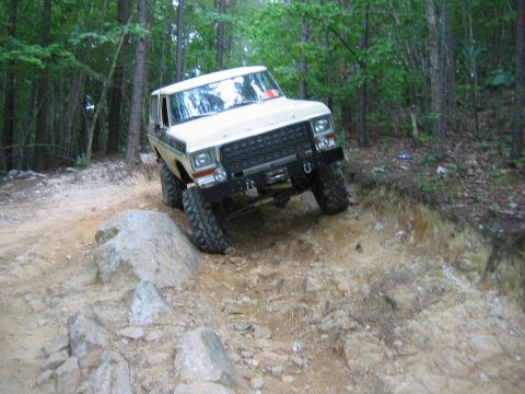 1992 Ford Mustang - A white Ford Bronco navigates a challenging rocky terrain on a wooded trail.