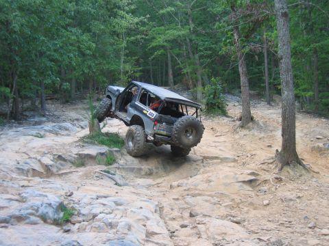 1992 Ford Mustang - Modified off-road vehicle navigates a challenging rocky trail in a forest setting.