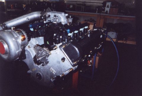 1992 Ford Crown Victoria - Assembled V8 engine on a stand in a shop, fitted with a positive-displacement supercharger and cast intake elbow, blue-topped fuel injector…